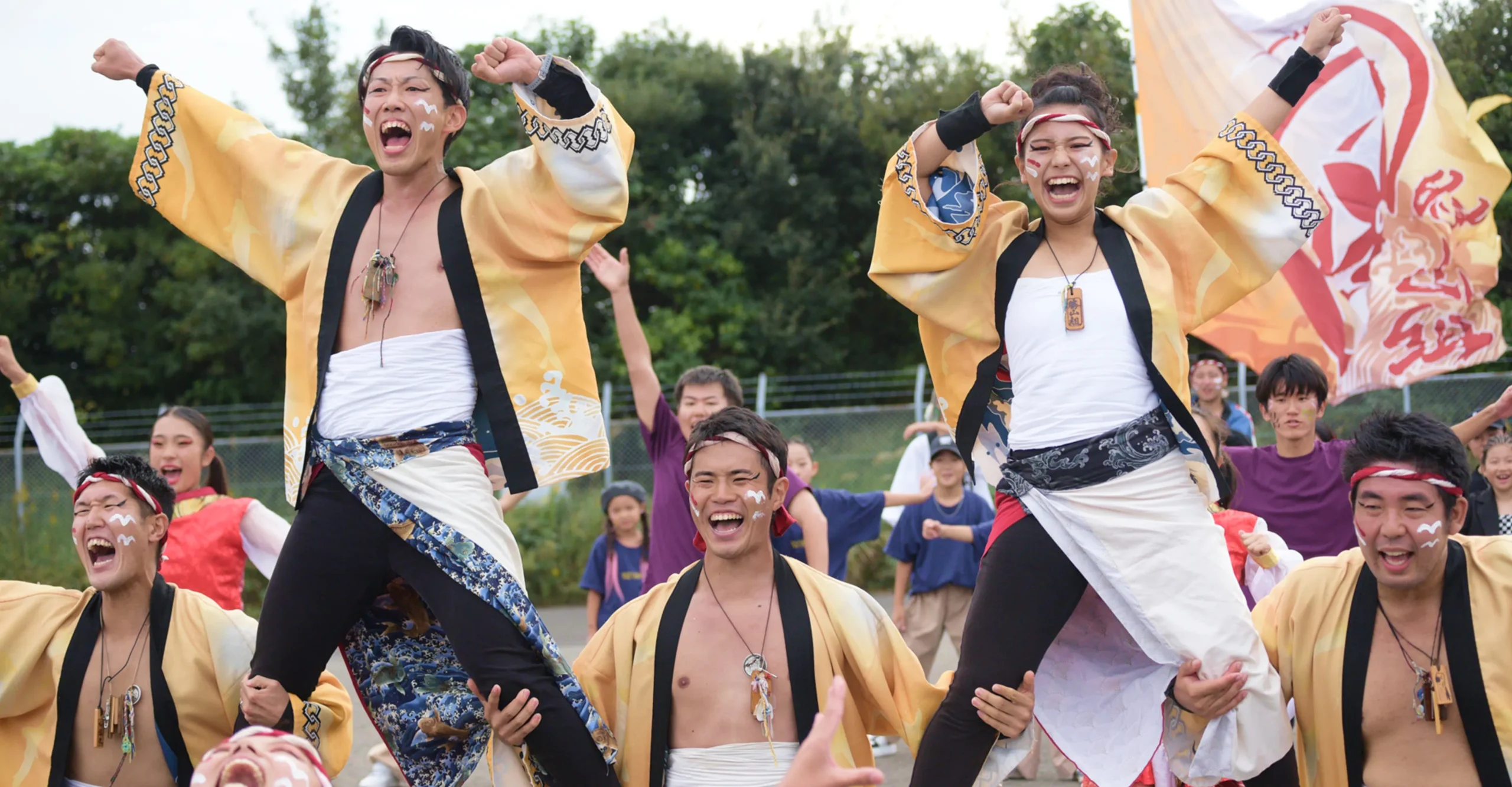 太鼓の音が鳴り響く中、法被を着た若者たちが笑顔で力強く踊る、活気あふれる祭りの一場面