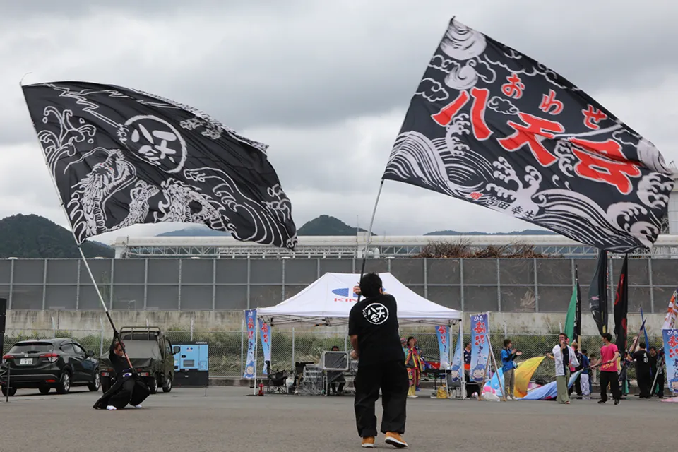 大きな旗を振るパフォーマーと屋外イベント会場の様子